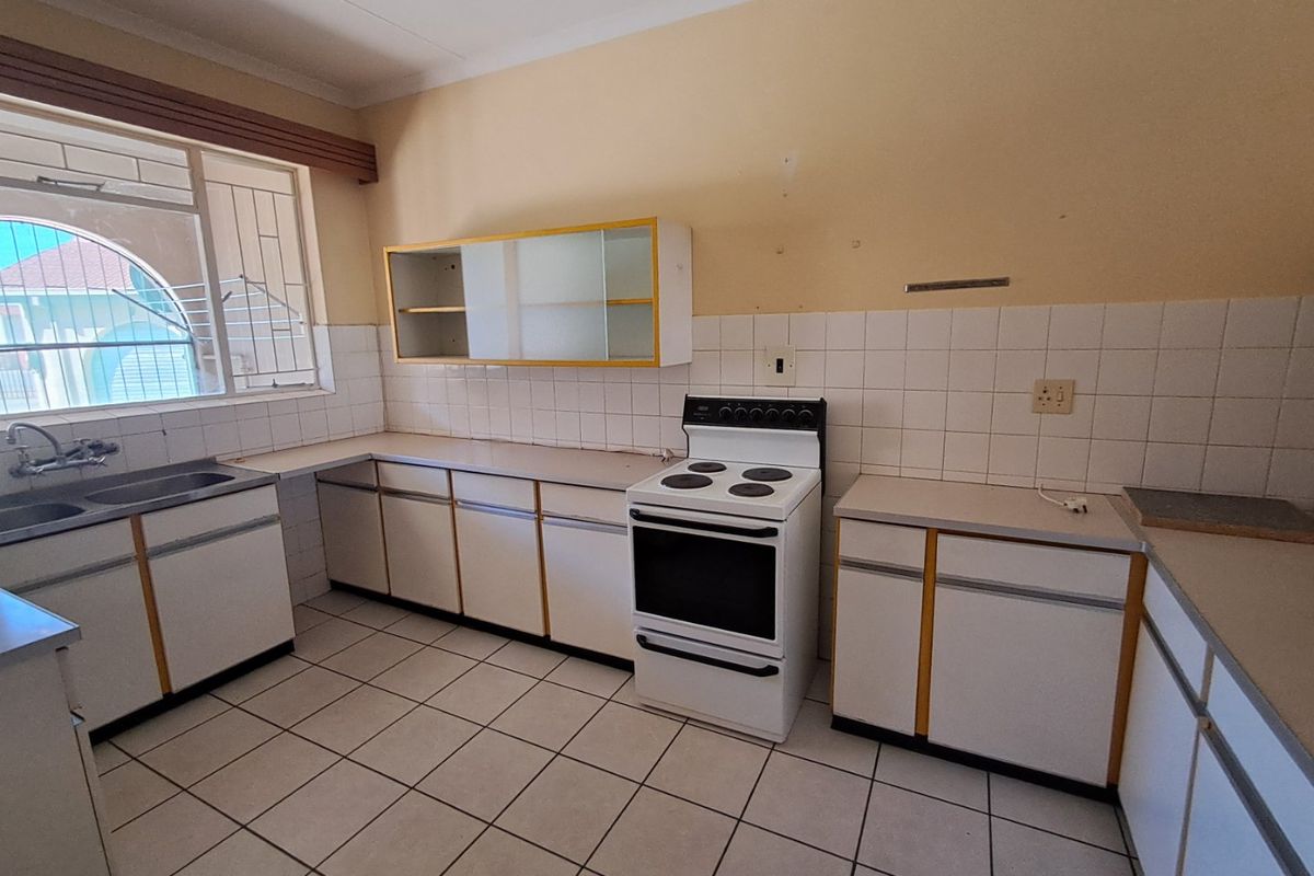 A functional, dated kitchen featuring white cabinetry, tiled flooring, and a freestanding electric stove, offering a blank canvas for modern renovation.