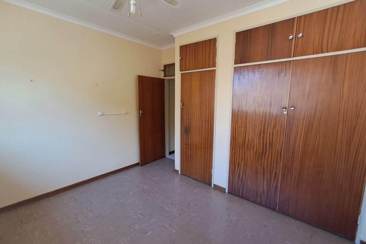 A vacant bedroom featuring built-in wooden cupboards, a ceiling fan, and vinyl flooring, offering a blank canvas for renovation or restyling.