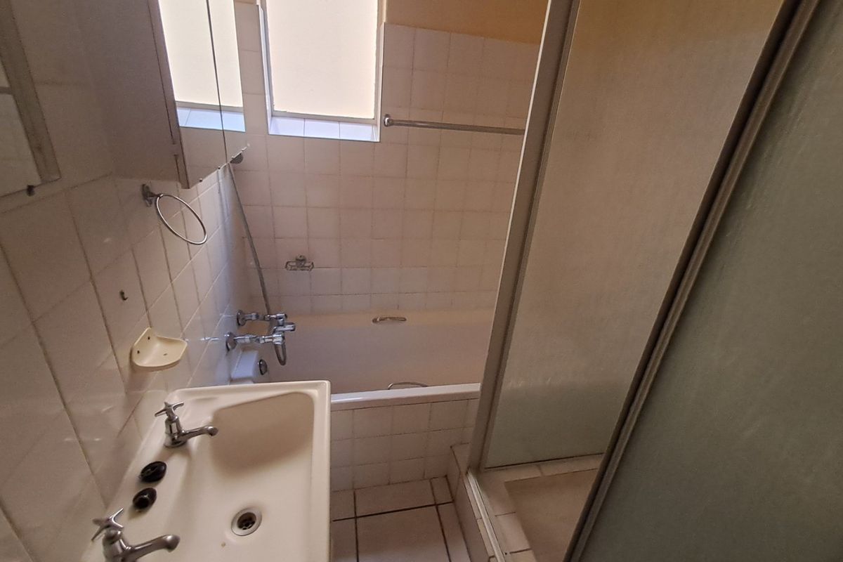A dated bathroom featuring a bathtub, separate shower enclosure, and pedestal basin with original wall and floor tiling.