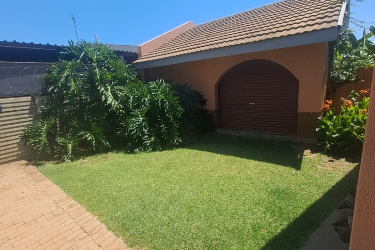 A well-maintained rear garden area featuring a paved walkway, manicured lawn, and a detached garage with a roller shutter door.