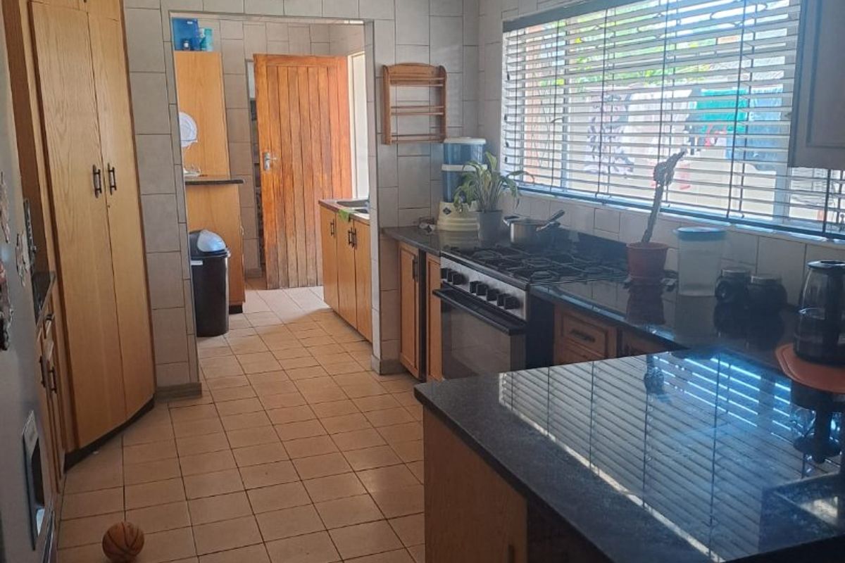 A functional kitchen featuring wooden cabinetry, granite countertops, a gas stove, and tiled finishes, with an adjacent scullery area visible through the doorway.