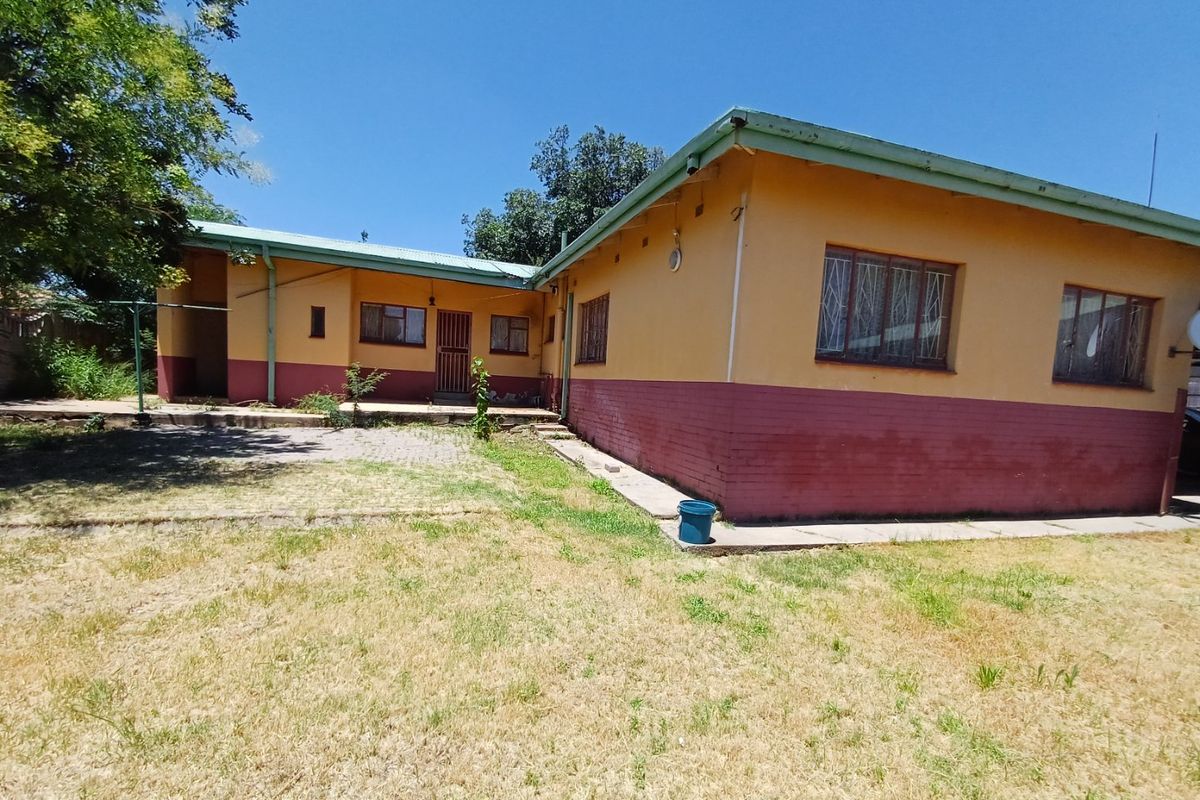Rear view of the house featuring a paved patio area, security bars on windows, and a large garden space.
