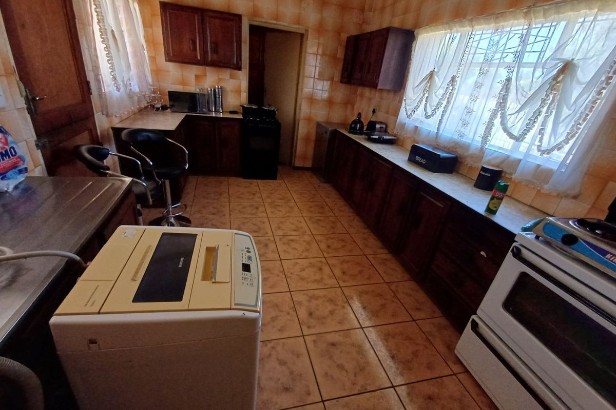 A dated kitchen featuring extensive wooden cabinetry, tiled wall finishes, and tiled flooring, offering a functional layout with potential for modern renovation.