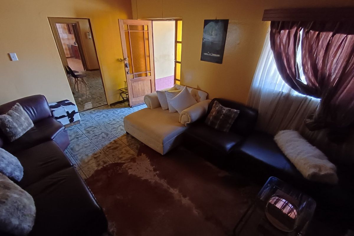 A living room area featuring tiled flooring and access to an adjacent room, with dated finishes and warm lighting.