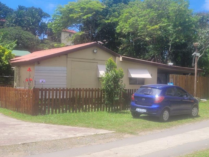 Front elevation of a townhouse featuring a timber picket fence, metal roofing, and window awnings, set within a landscaped residential environment.