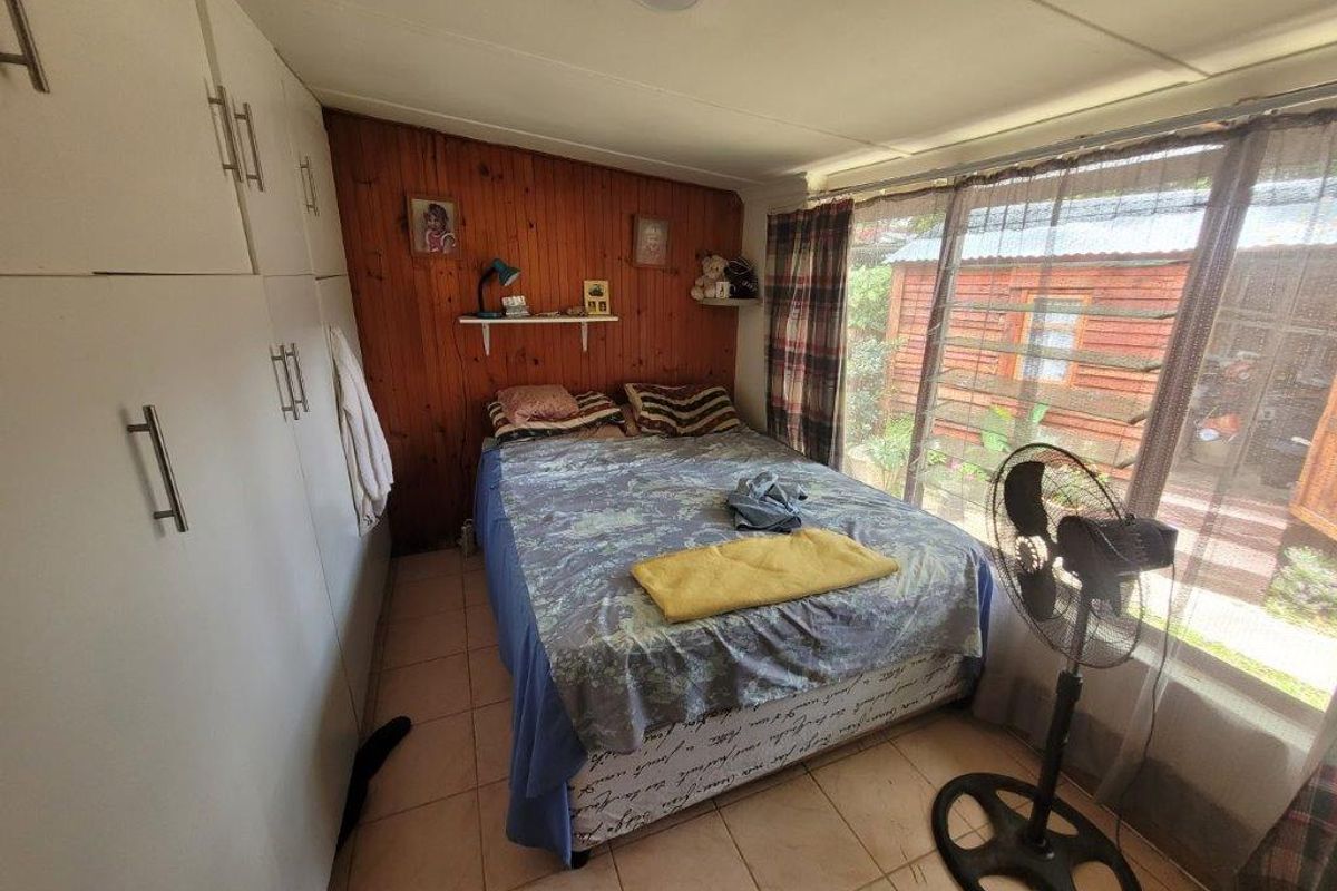 Bedroom featuring built-in cupboards, tiled flooring, and wood paneling, with large windows providing natural light and garden views.