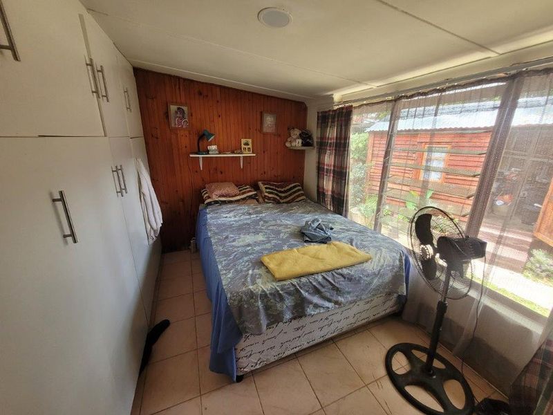 Bedroom featuring built-in cupboards, tiled flooring, and wood paneling, with large windows providing natural light and garden views.