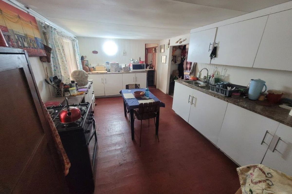 A dated kitchen featuring white cabinetry, laminate countertops, a stainless steel sink, and timber flooring, offering potential for a modern renovation.