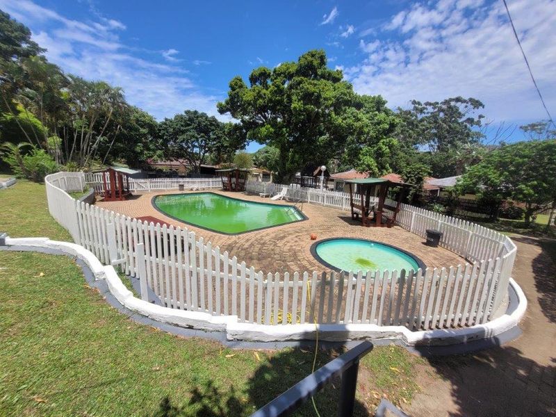 Communal pool area featuring a main swimming pool and a smaller wading pool, enclosed by a white picket fence with paved surround.
