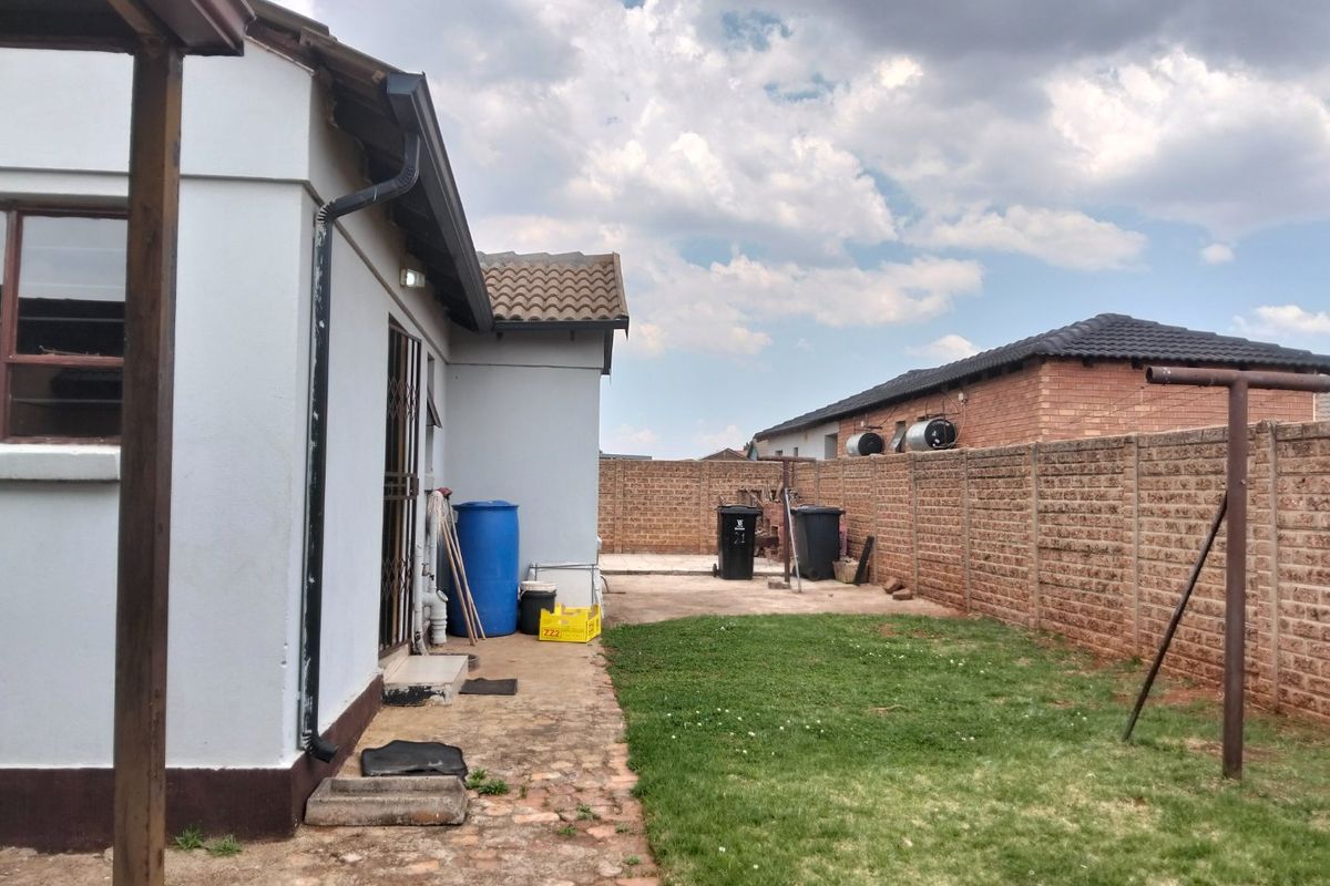 Rear exterior view of the property featuring a small lawn, concrete patio area, and brick boundary walling.