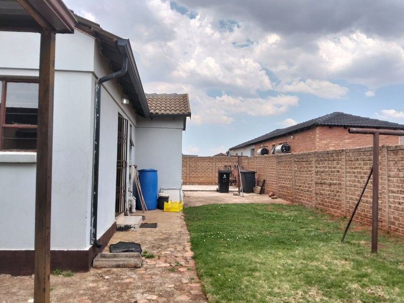 Rear exterior view of the property featuring a small lawn, concrete patio area, and brick boundary walling.