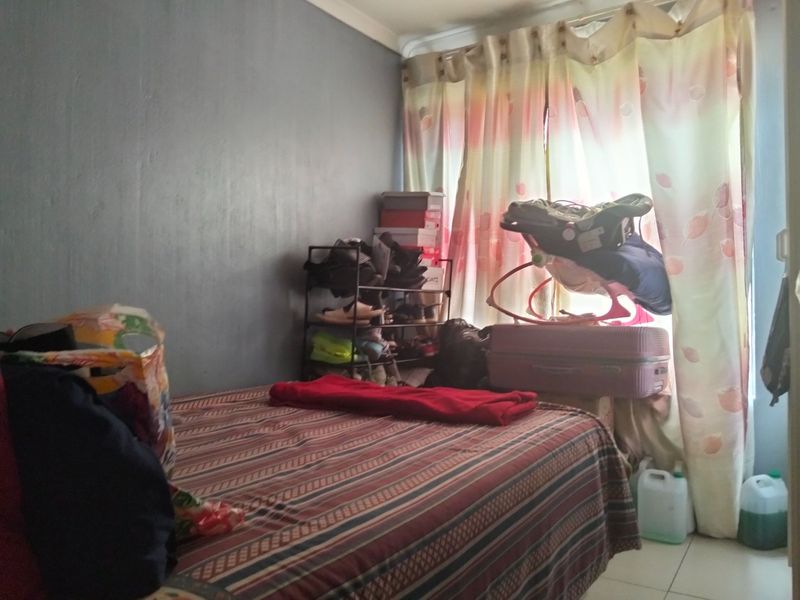 A compact bedroom featuring tiled flooring and window curtain treatments, offering a functional space for rest.