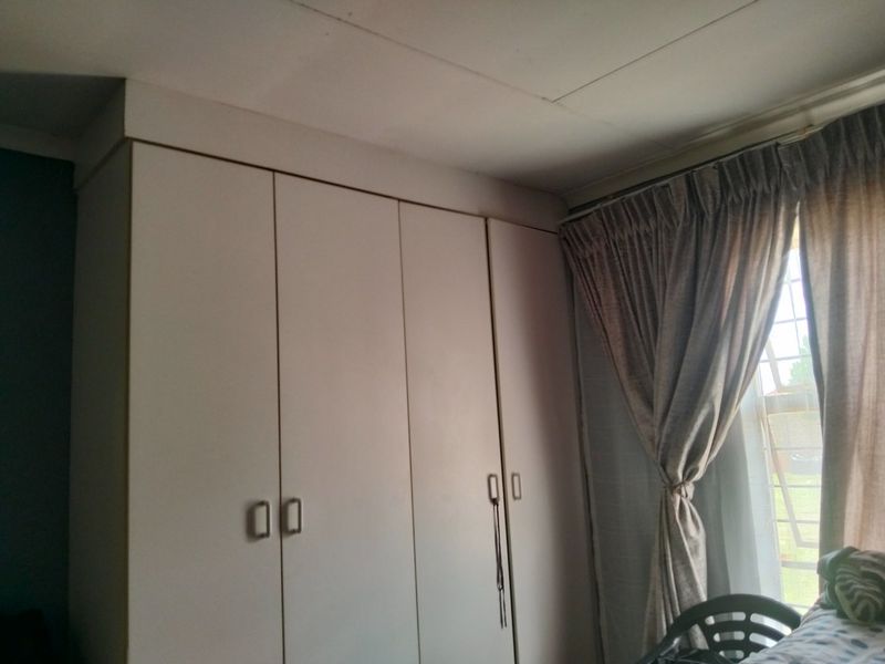 A bedroom featuring built-in cupboards and a window with security bars, showing standard finishes and typical wear.