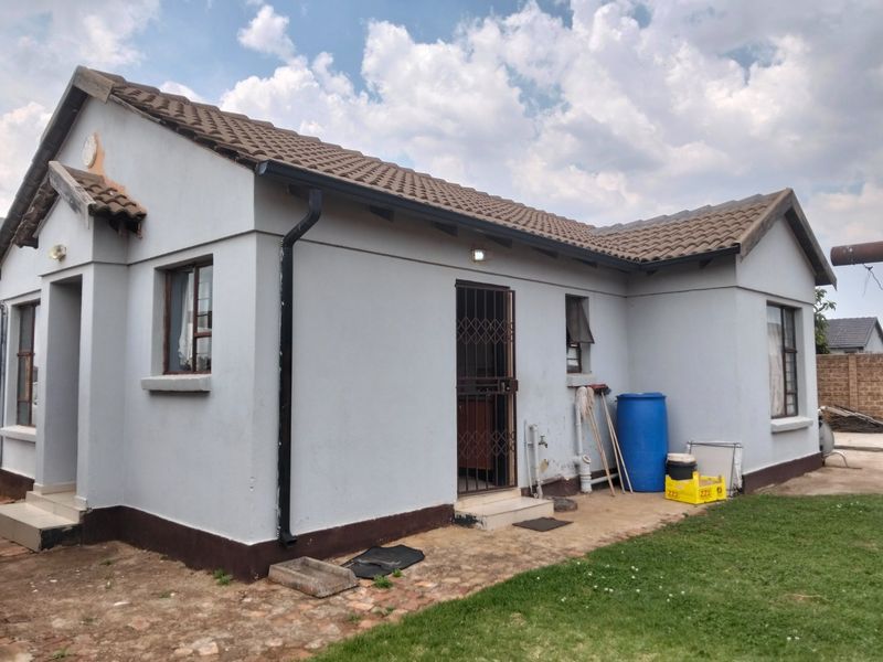 Rear view of a single-story house featuring a tiled roof, security gate, and concrete apron, showing standard exterior finishes and maintenance requirements.