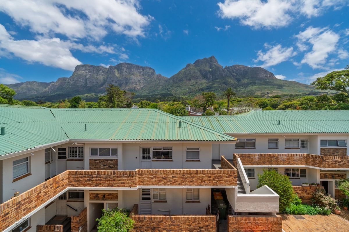 An elevated view of the apartment complex rear facade featuring face brick construction, green corrugated metal roofing, and a scenic mountain backdrop.