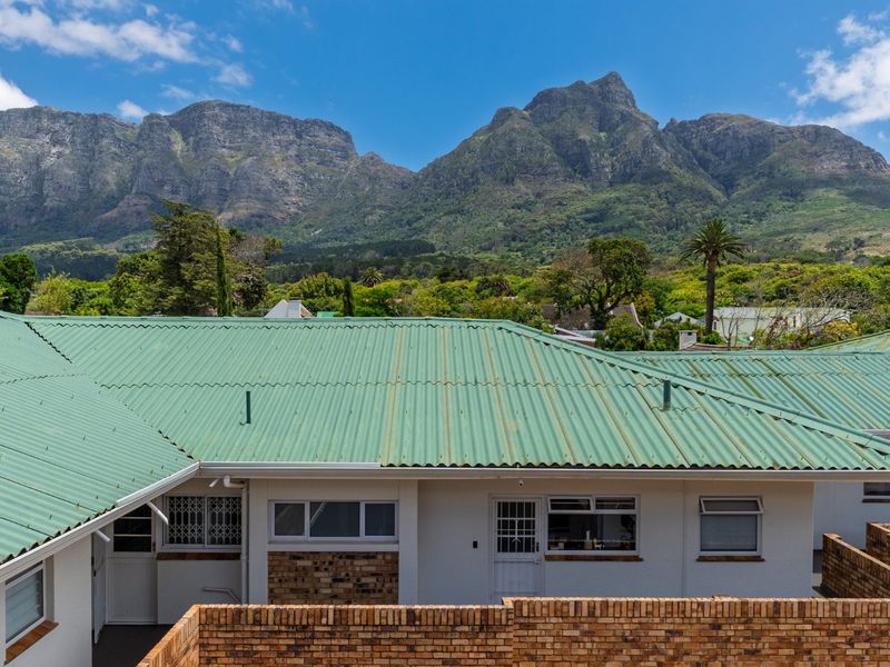 Rear view of the apartment building featuring a corrugated metal roof and brick boundary wall, set against a scenic mountain backdrop.