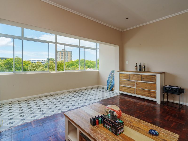 Spacious living area featuring a combination of parquet and patterned tile flooring, large windows providing natural light, and neutral wall finishes.
