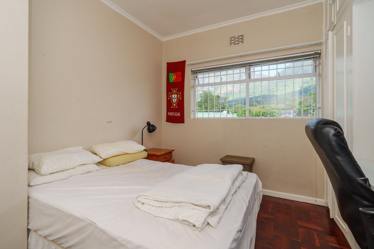 A bedroom featuring parquet flooring, built-in cupboards, and a window with security bars offering a mountain view.