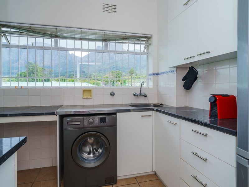 A functional kitchen featuring built-in cabinetry, dark laminate countertops, a stainless steel sink, and a window with security bars overlooking mountain views.