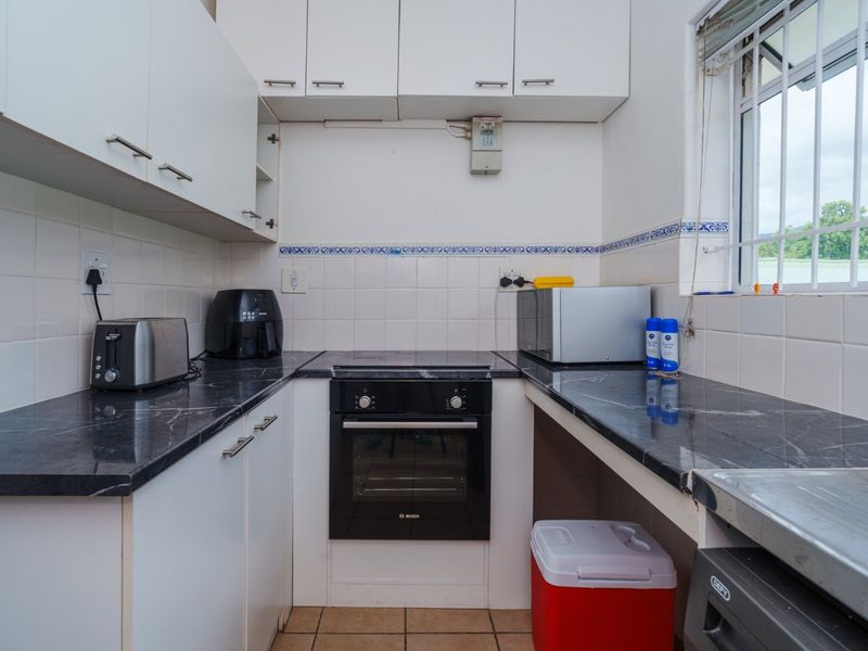 Compact kitchen featuring white cabinetry, dark laminate countertops, built-in oven, ceramic hob, and tiled backsplash with a window providing natural light.
