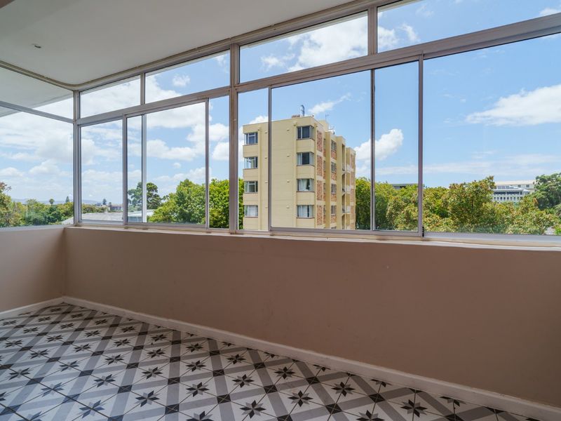A bright, enclosed balcony featuring large glass windows and decorative patterned floor tiles, offering an open view of the surrounding neighborhood.
