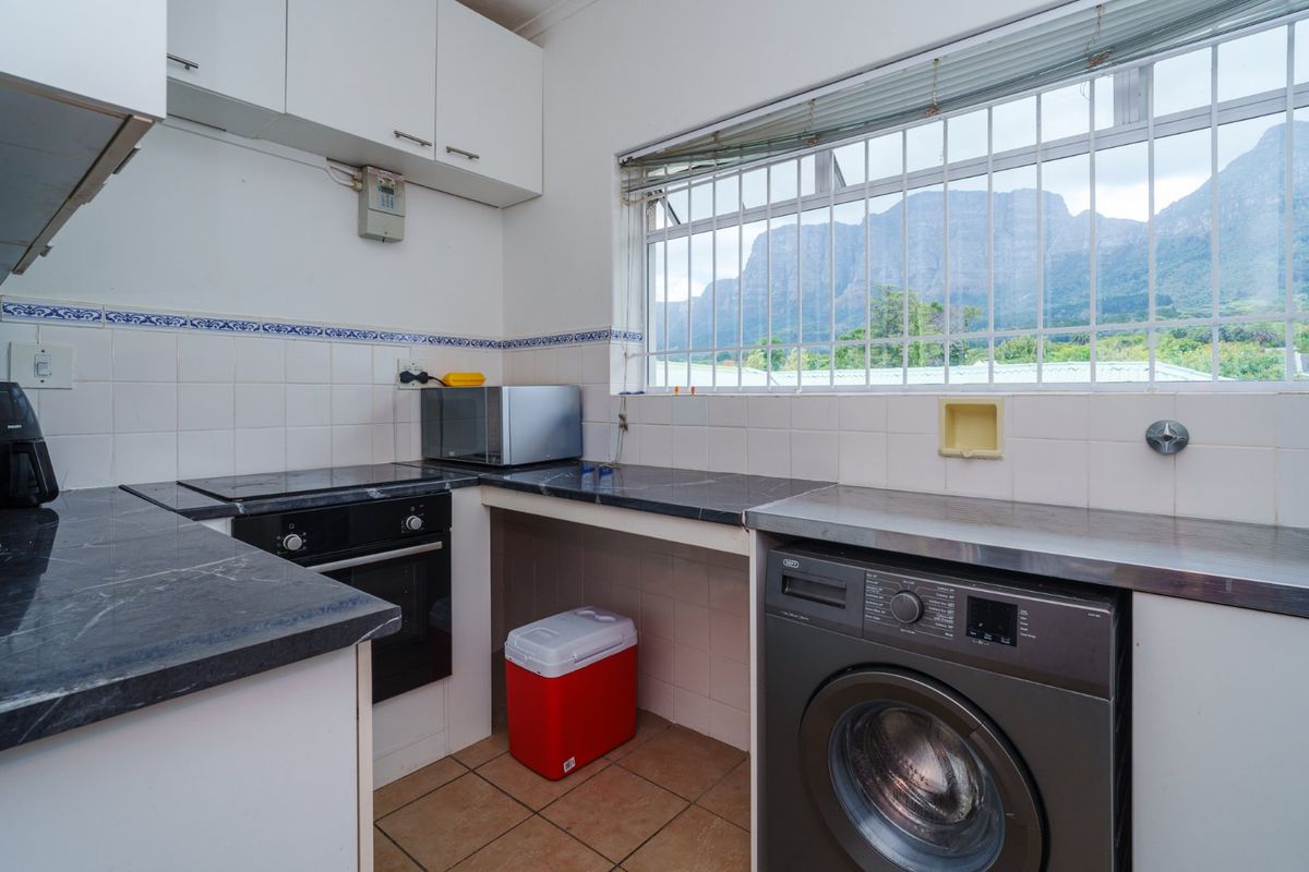 Functional kitchen featuring built-in cabinetry, dark laminate countertops, integrated oven and hob, tiled backsplash, and a window with security bars overlooking mountain views.