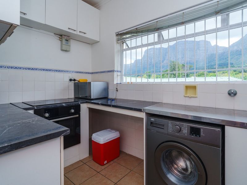 Functional kitchen featuring built-in cabinetry, dark laminate countertops, integrated oven and hob, tiled backsplash, and a window with security bars overlooking mountain views.