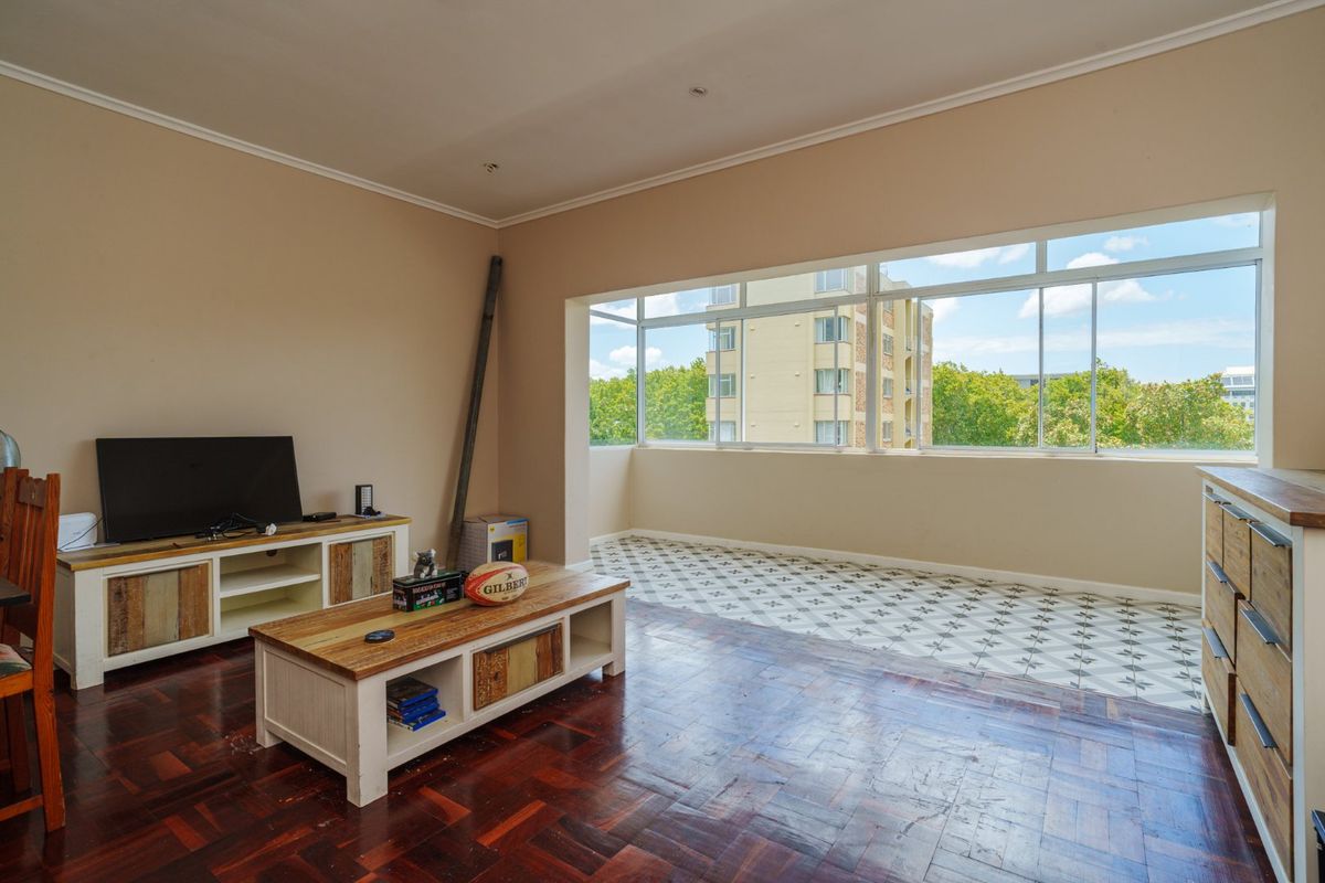 Spacious living area featuring a combination of classic parquet and decorative tiled flooring, large windows providing ample natural light, and neutral wall finishes.