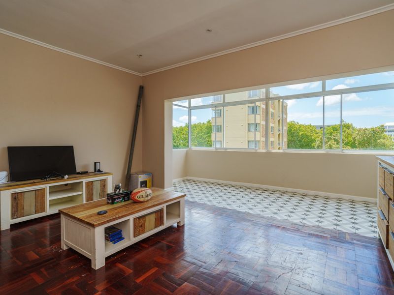 Spacious living area featuring a combination of classic parquet and decorative tiled flooring, large windows providing ample natural light, and neutral wall finishes.
