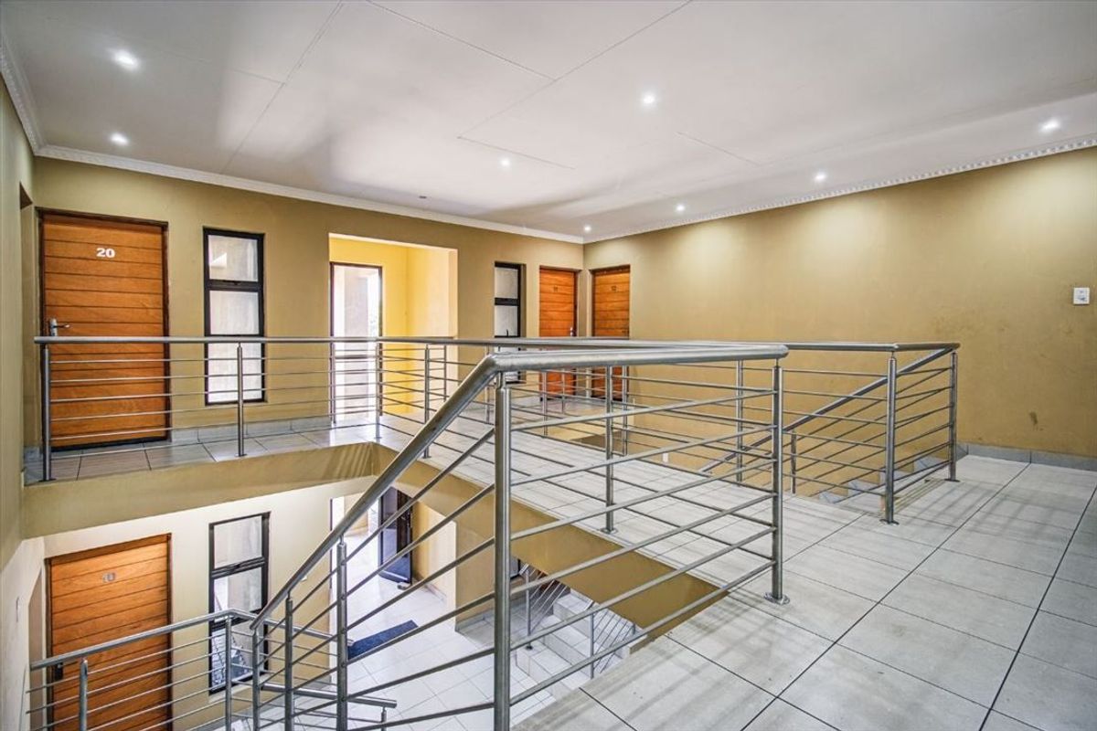 A well-maintained multi-level hallway featuring tiled flooring, stainless steel balustrades, and multiple access doors to individual units.