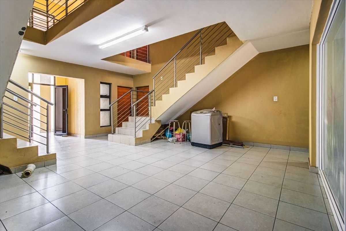 Spacious entrance hall featuring a central staircase with stainless steel balustrades and neutral tiled flooring, offering a functional and open layout.