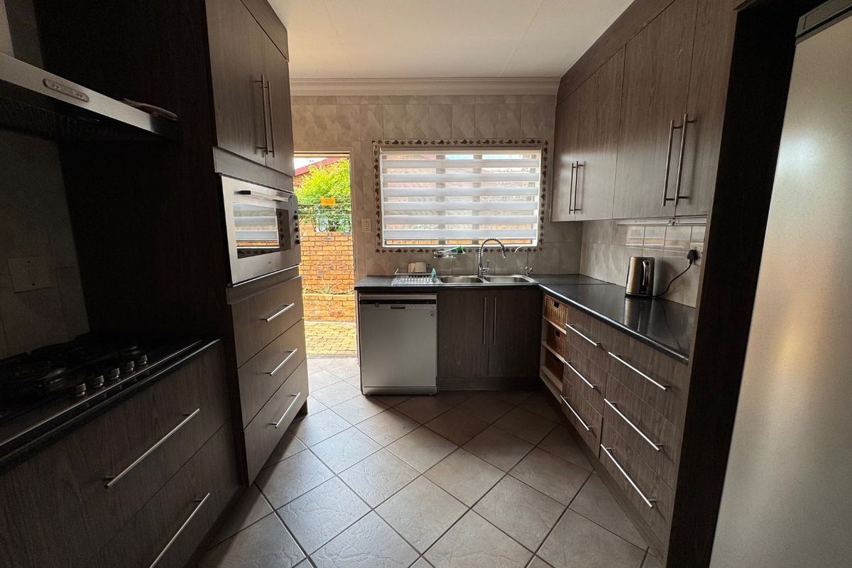 A functional kitchen featuring dark wood cabinetry, granite-look countertops, built-in oven, gas hob, and tiled flooring with direct access to the rear exterior.