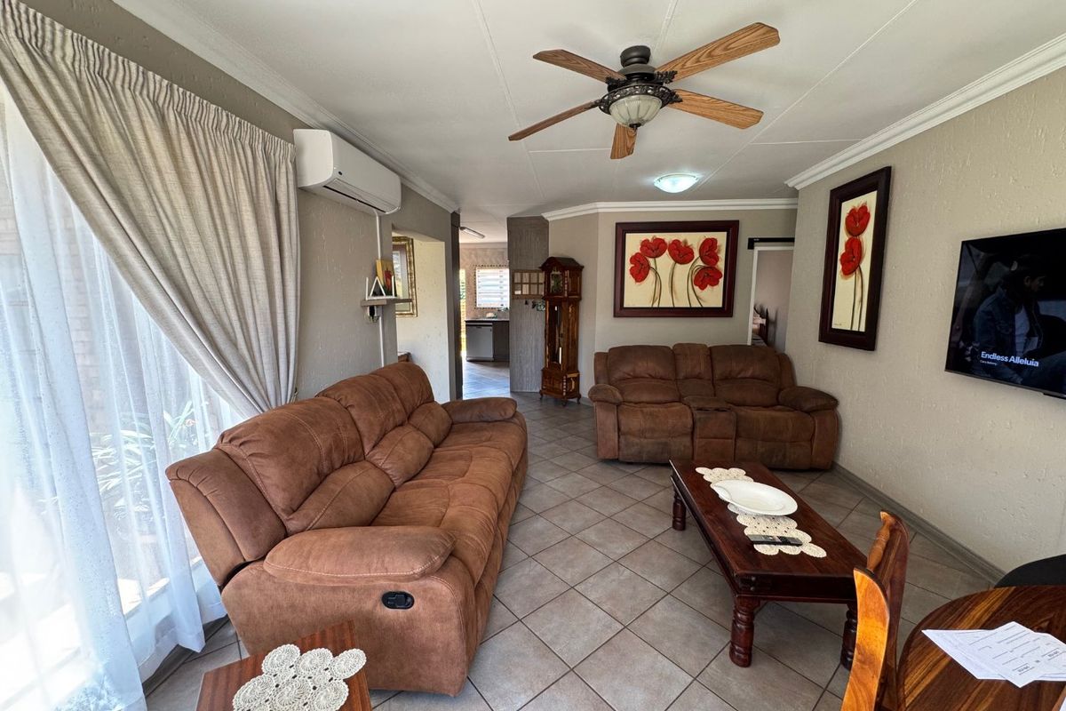 A comfortable living room featuring tiled flooring, a ceiling fan, and a split-system air conditioner, with direct access to an outdoor area via sliding doors.