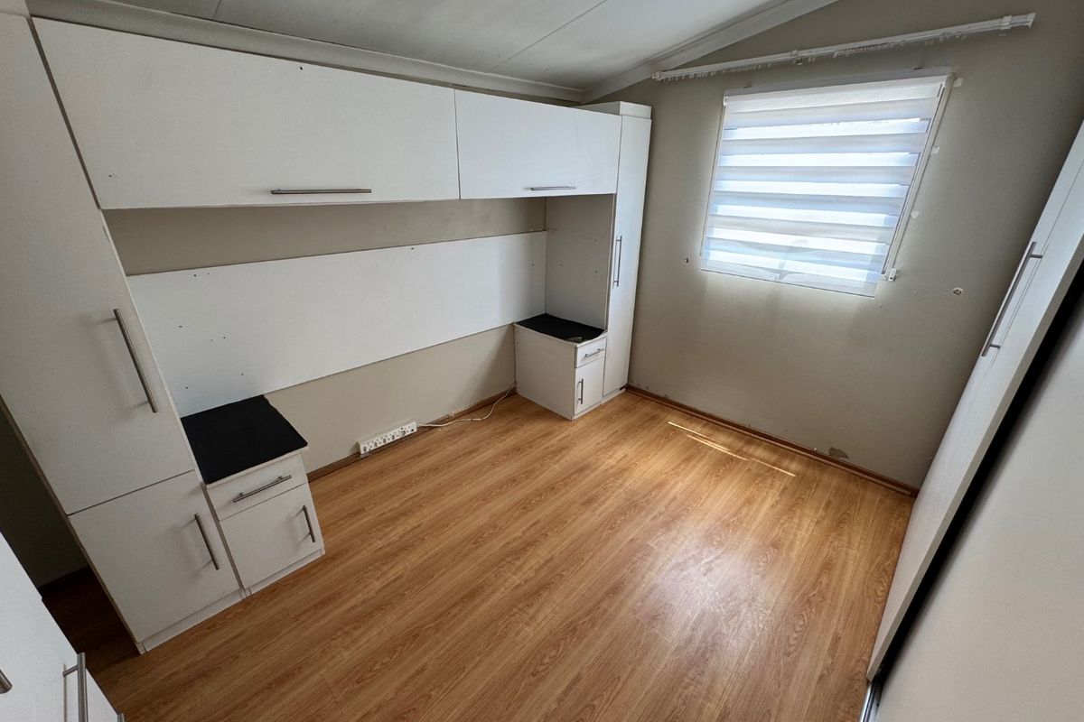 A vacant bedroom featuring built-in cabinetry, laminate flooring, and a window with roller blinds, offering a functional space ready for personalization.