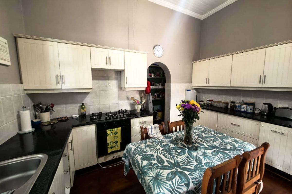 A functional kitchen featuring white cabinetry, black granite countertops, a gas hob, and a convenient walk-in pantry archway.