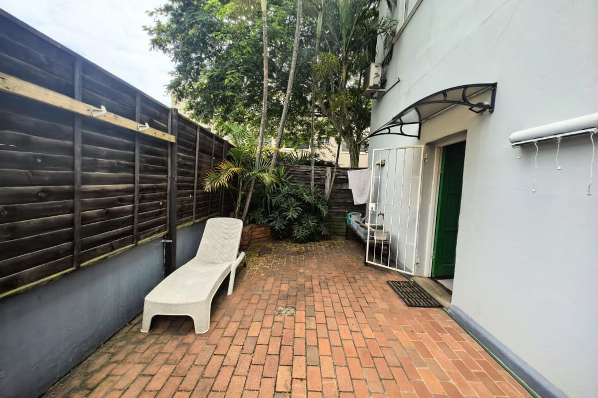A private rear courtyard featuring brick paving, a timber boundary fence, and direct access to the apartment via a security gate.