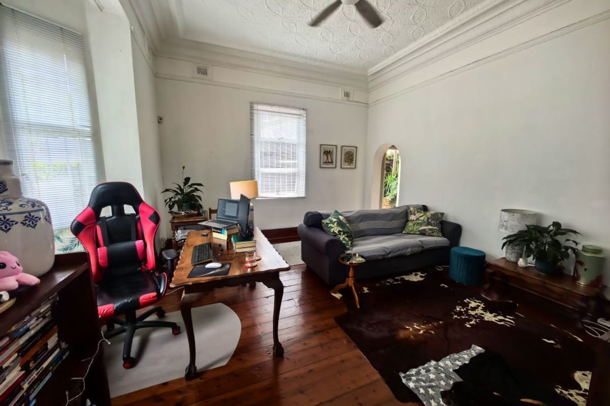 A living room featuring original hardwood floors, a decorative ceiling with a fan, and an arched doorway leading to an adjacent space.