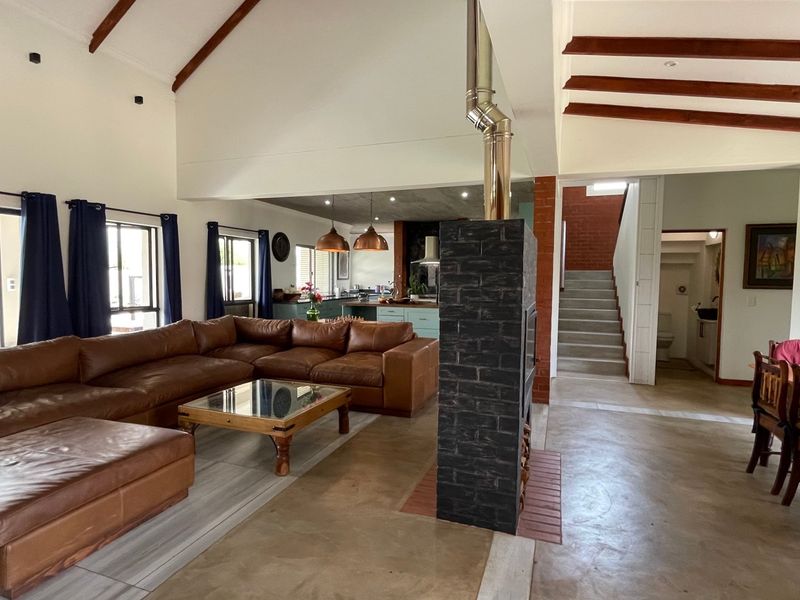 Spacious open-plan living area featuring vaulted ceilings with exposed timber beams, a central brick fireplace, and polished concrete flooring leading to the kitchen.