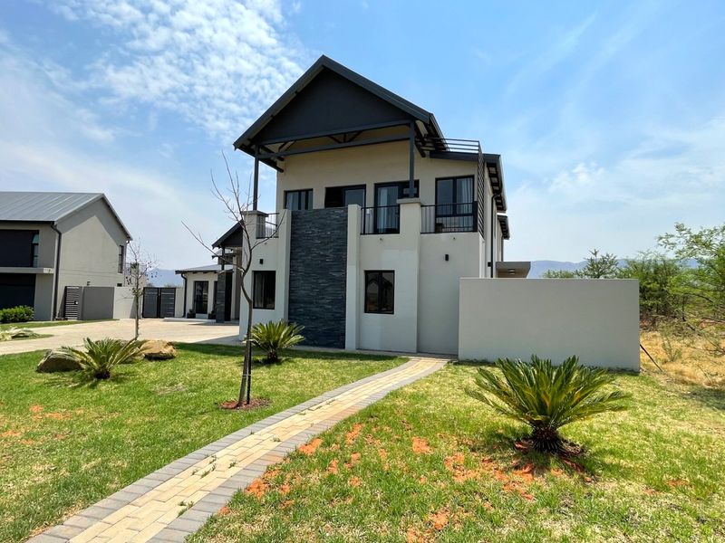 Modern two-story residential home featuring a stone-clad facade, balcony, and paved walkway set within a landscaped estate environment.