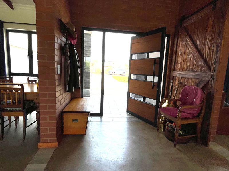 Welcoming entrance hall featuring exposed brickwork, polished concrete floors, timber ceiling beams, and a modern pivot front door leading to the exterior.