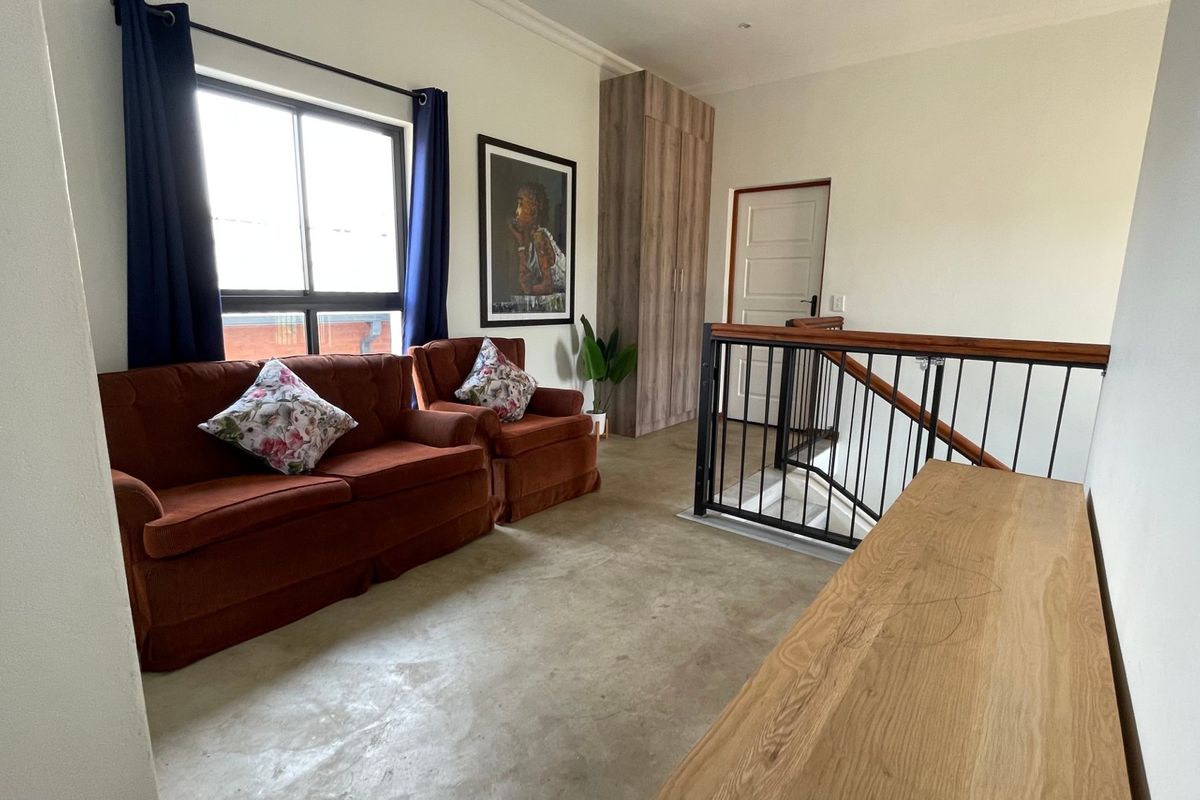 A bright living area featuring polished concrete floors, a built-in cupboard, and a staircase with a wooden handrail and metal balustrade.