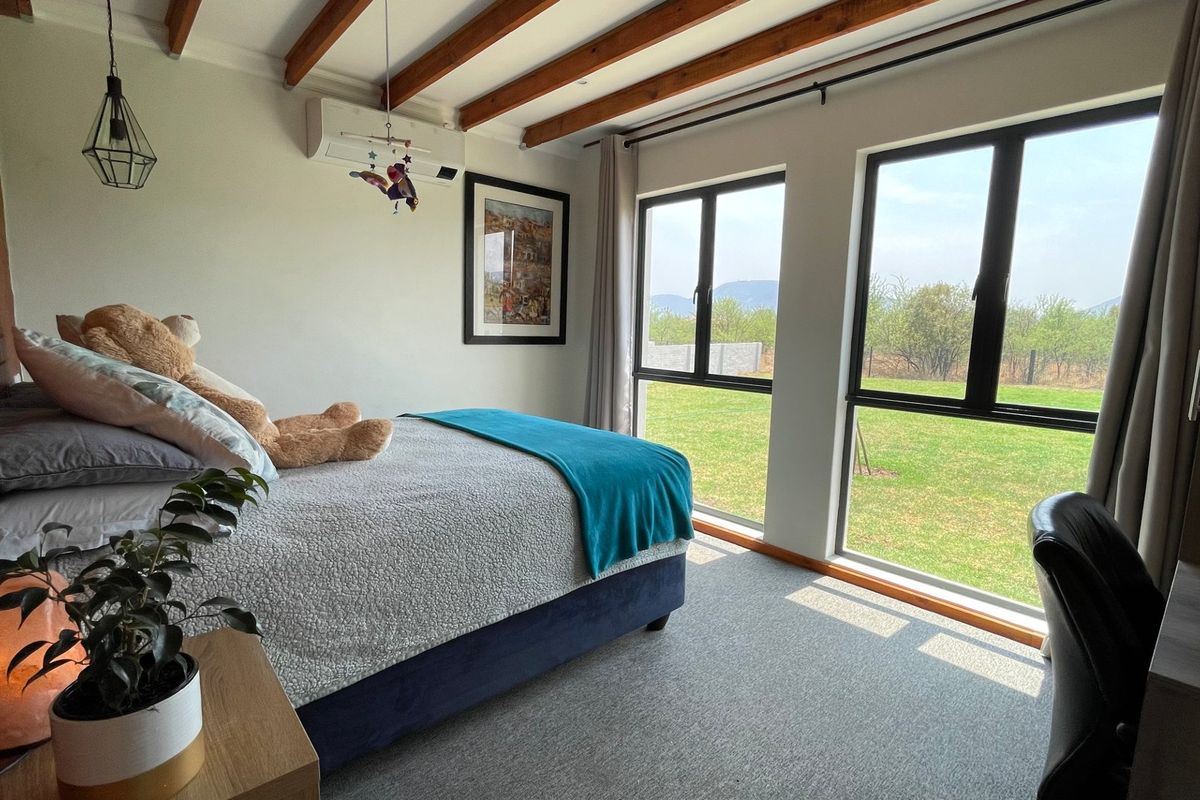 A well-maintained bedroom featuring exposed timber ceiling beams, an exposed brick wall, and large windows providing natural light and garden views.