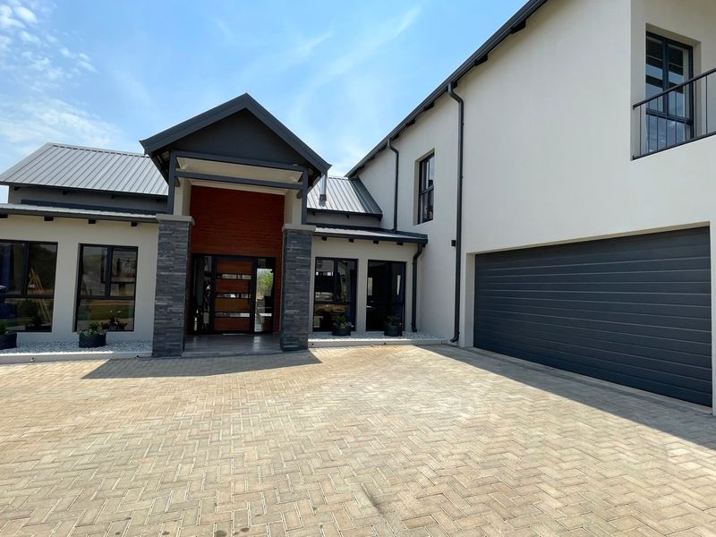 Modern double-story residence featuring a paved driveway, double garage, stone-clad entrance, and a balcony, showcasing contemporary architectural design.