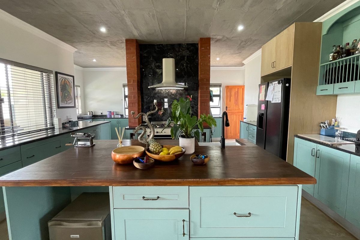 Spacious kitchen featuring a large central island with a wooden countertop, custom cabinetry, and a distinctive exposed brick pillar with a modern extractor fan.