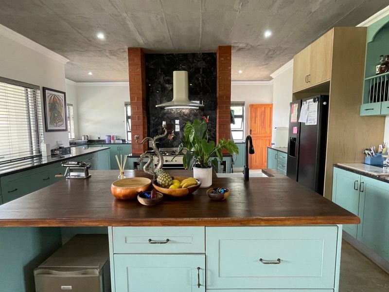 Spacious kitchen featuring a large central island with a wooden countertop, custom cabinetry, and a distinctive exposed brick pillar with a modern extractor fan.