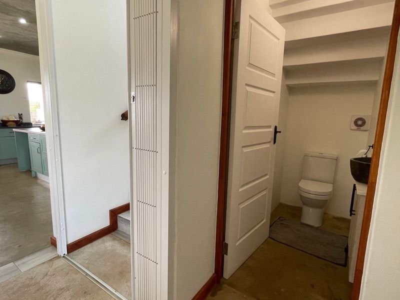 A hallway view showing a small guest bathroom with a toilet and vanity, adjacent to an open-plan kitchen area.