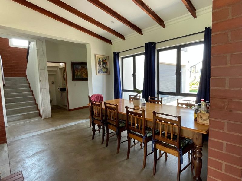 Spacious dining area featuring exposed timber ceiling beams, polished concrete floors, and an exposed brick feature wall with natural light from large windows.