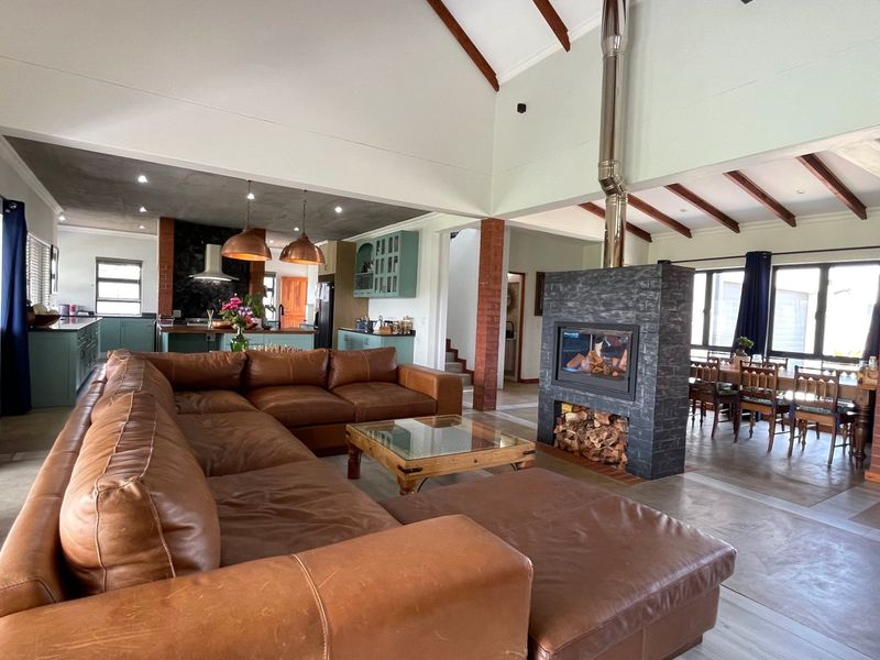 Spacious open-plan living area featuring a vaulted ceiling with exposed beams, a central stone fireplace, and polished concrete floors, seamlessly connecting to the kitchen.