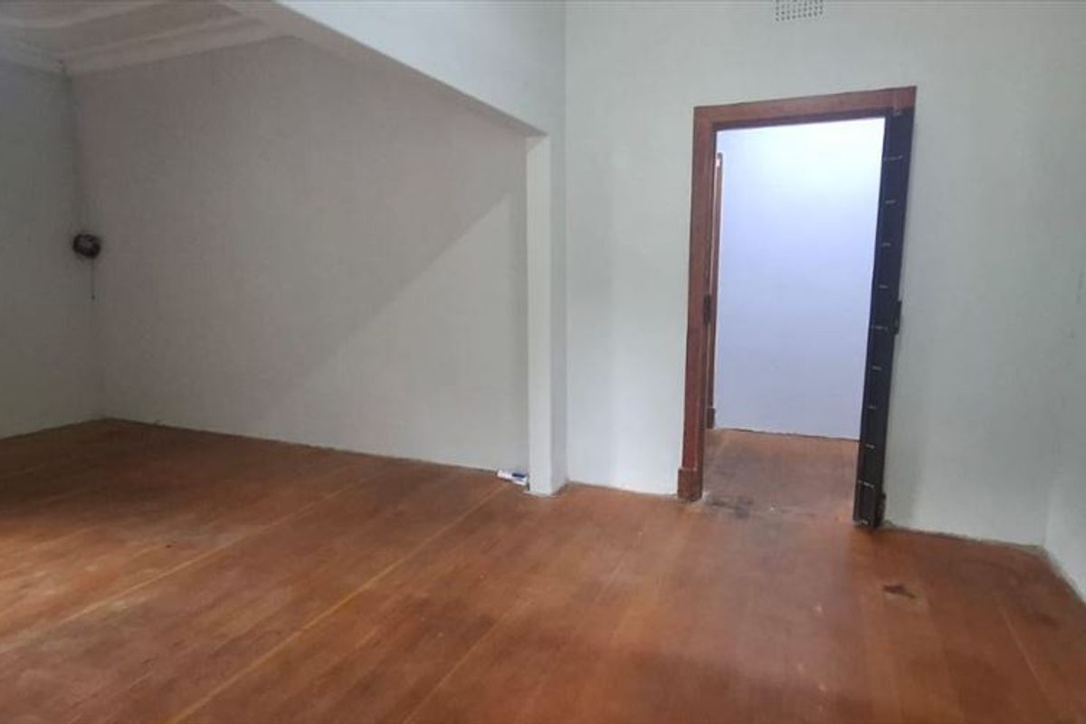 An empty living room featuring original hardwood flooring, coved ceilings, and a timber door frame leading to an adjacent space.