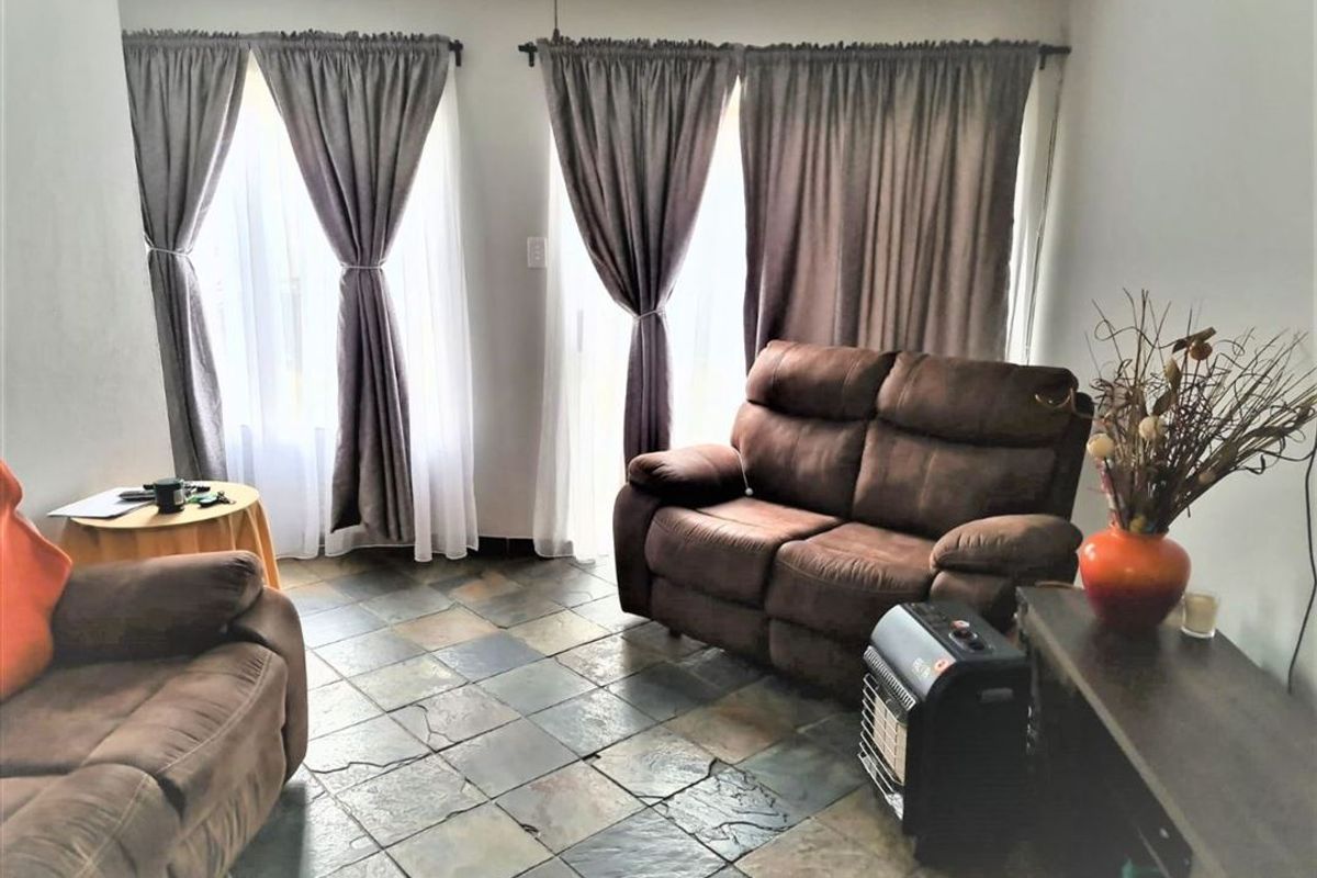 A living room featuring natural stone tile flooring and large windows with curtain treatments, providing a functional and lived-in space.
